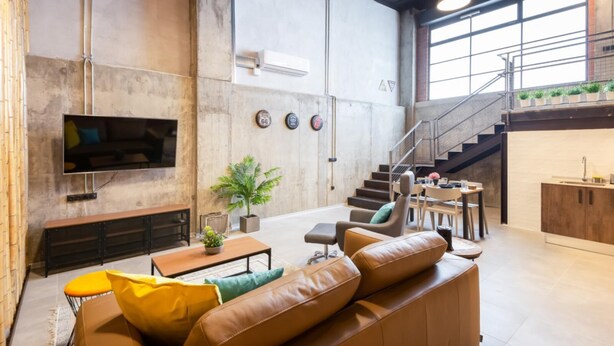 A spacious living area with a large sofa, a coffee table, and a TV mounted on the wall. There is a staircase leading to an upper level with a balcony. - Art Loft 06 'Travelling Light' in Valencia (València)
