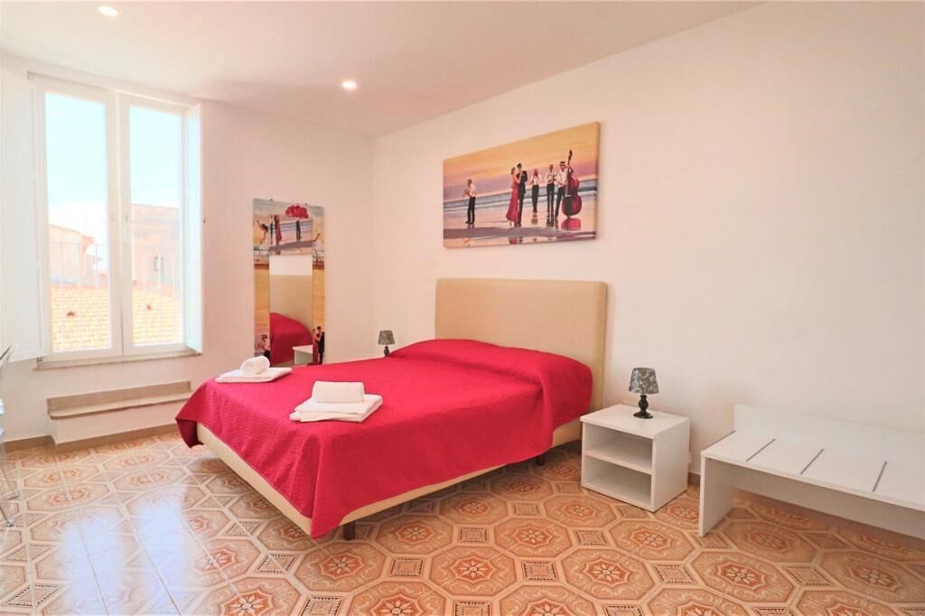 Une chambre d’hôtel avec un grand lit, une petite table de chevet, une commode, une fenêtre donnant sur un beau paysage et un tableau au mur.