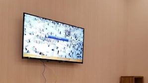 A television mounted on a wall above a wooden entertainment center with drawers and shelves.