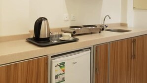 A kitchenette with wooden cabinets, a coffee maker, a kettle, a toaster, and a small refrigerator.