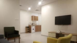A living room with a sofa, a yellow armchair, and a flat-screen TV mounted on the wall.