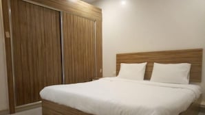 A bedroom with a wooden bed frame, white bedding, and a wooden wardrobe.