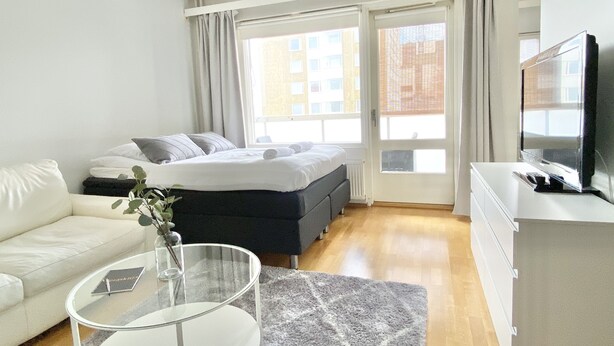 A modern hotel room with a bed, a sofa, a TV, and a window with curtains. - City Home Finland Laukontori (Tampere)