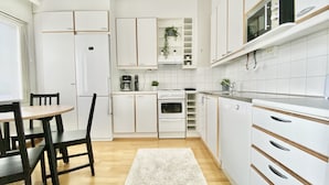 A modern kitchen with white cabinets, a dining table with chairs, and a white rug. - City Home Finland Laukontori (Tampere)