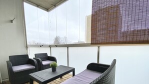 A balcony with wicker furniture, including two chairs and a small table, and a view of the city through large windows. - City Home Finland Laukontori (Tampere)