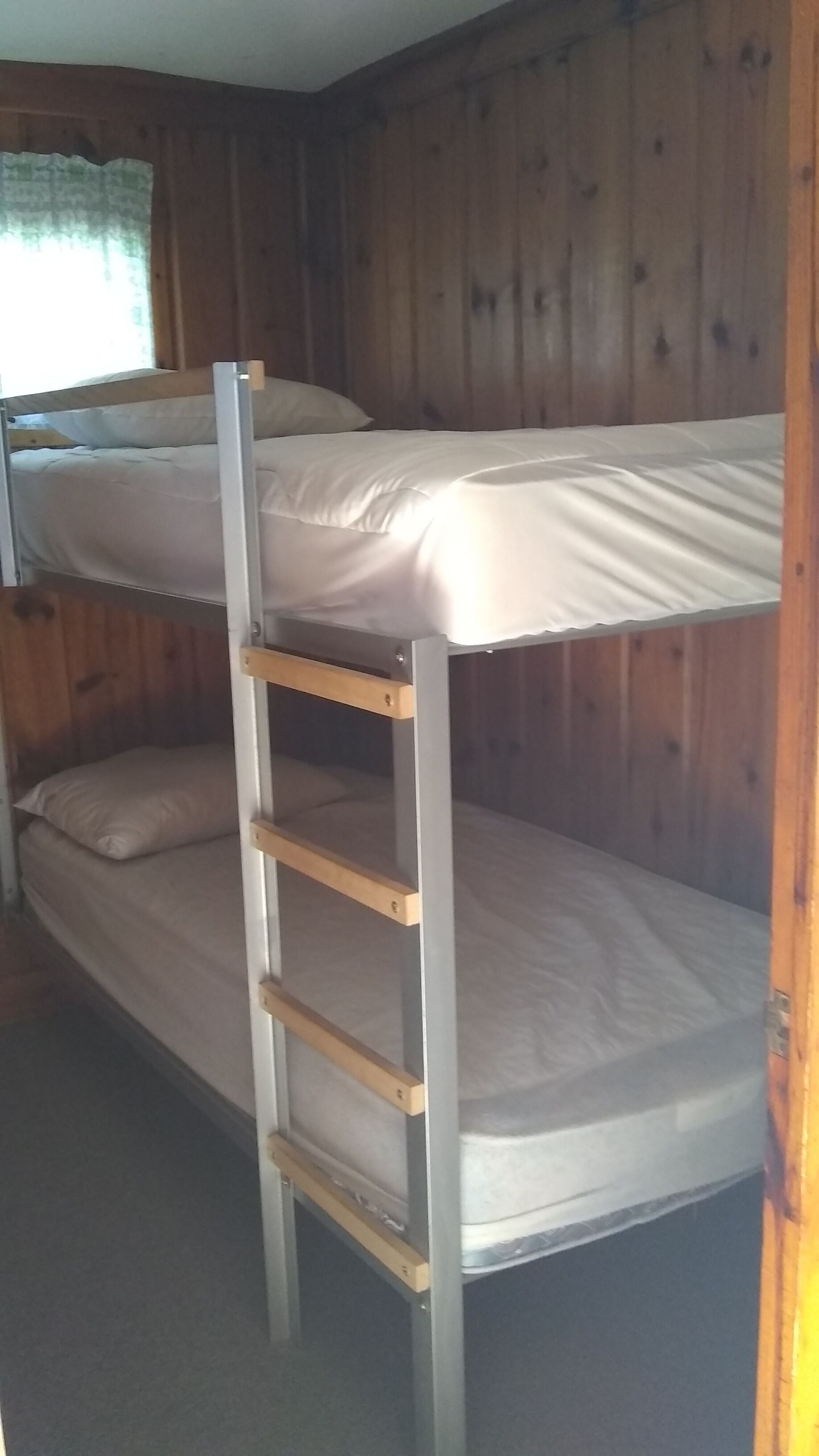 Un letto a castello con una scala, pareti in legno e una finestra con tende.