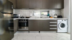 Una cucina moderna con elettrodomestici in acciaio inossidabile, forno integrato, lavatrice e una finestra con persiane.