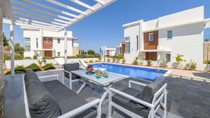 Area piscina moderna all'aperto con pergola, posti a sedere e cielo azzurro.