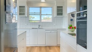 A modern kitchen with white cabinetry, a built-in dishwasher, a double sink, and a window with a view of the outside. - Albacore 7, 12 Ondine Close, Waterfront Unit with (Nelson Bay)