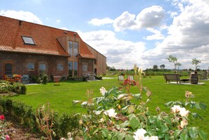 A brick building with a sloped roof, a grassy lawn, and outdoor seating.