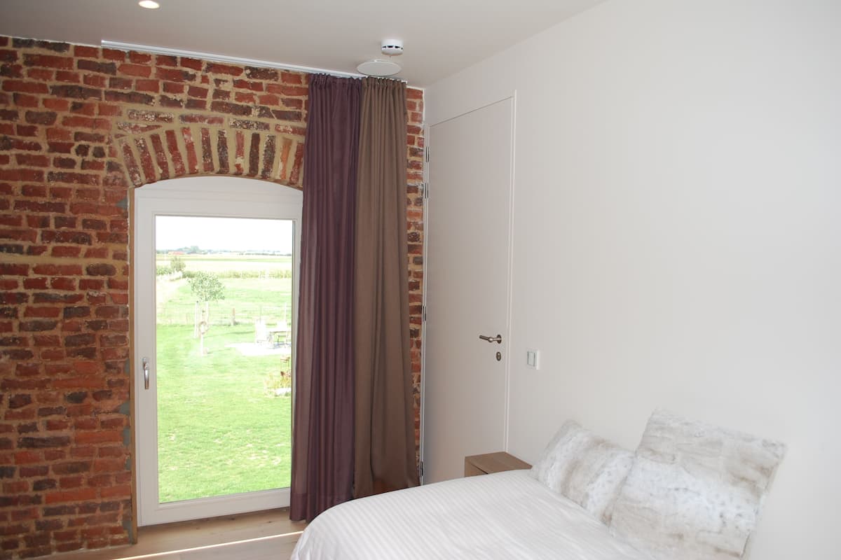 A bedroom with a brick wall, a door leading to a balcony, and a bed with white bedding.
