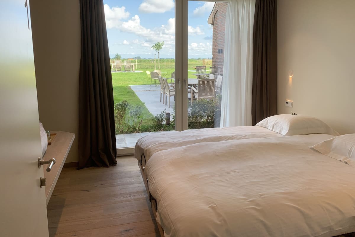 A bedroom with a large bed, a wooden dresser, and a sliding glass door leading to a patio with outdoor furniture.