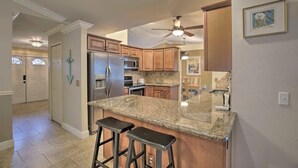 A kitchen with granite countertops, stainless steel appliances, wooden cabinets, and a ceiling fan. - Cape Escape SW Florida (Cape Coral)