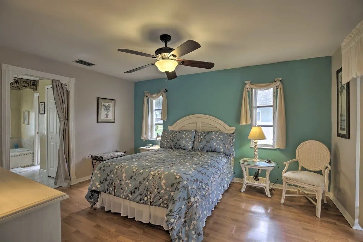 A bedroom with a bed, a chair, a nightstand, a ceiling fan, and a window with curtains.