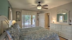 A bedroom with a bed, a ceiling fan, a dresser, a mirror, and a view of the outdoors. - Cape Escape SW Florida (Cape Coral)