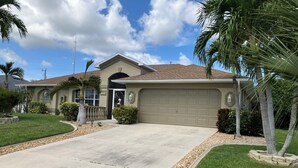 A residential house with a garage, a well-maintained lawn, and palm trees. - Cape Escape SW Florida (Cape Coral)