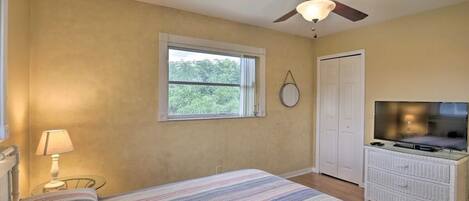 A bedroom with a bed, a ceiling fan, a TV, a dresser, a window, and a door.
