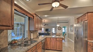 A spacious kitchen with granite countertops, wooden cabinets, a stainless steel refrigerator, and a ceiling fan. - Cape Escape SW Florida (Cape Coral)