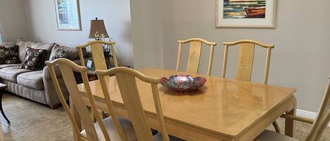 Un comedor con mesa y sillas de madera, un cuenco decorativo, un sofá con cojines estampados y un cuadro enmarcado en la pared.