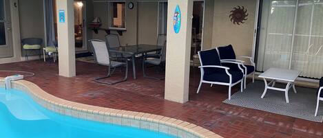 A covered outdoor area with a pool, patio furniture, and a dining table.