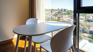 A room with a table and two chairs, a large window with a city view, and a curtain on the window. - Tamara Jeju (Seogwipo)