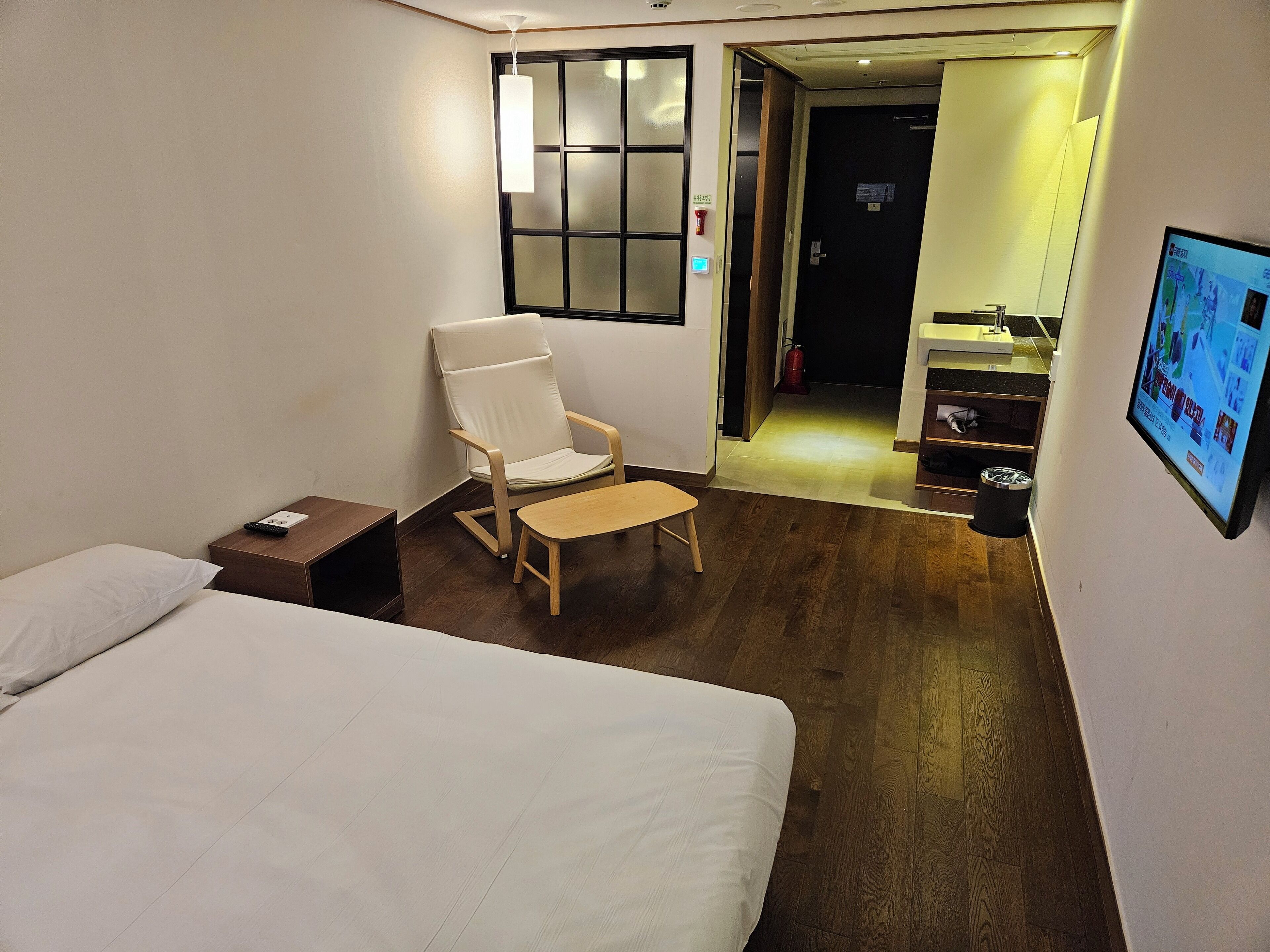 A hotel room with a bed, a chair, a small table, a TV, and a wooden floor.