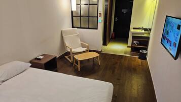 A hotel room with a bed, a chair, a small table, a TV, and a wooden floor.