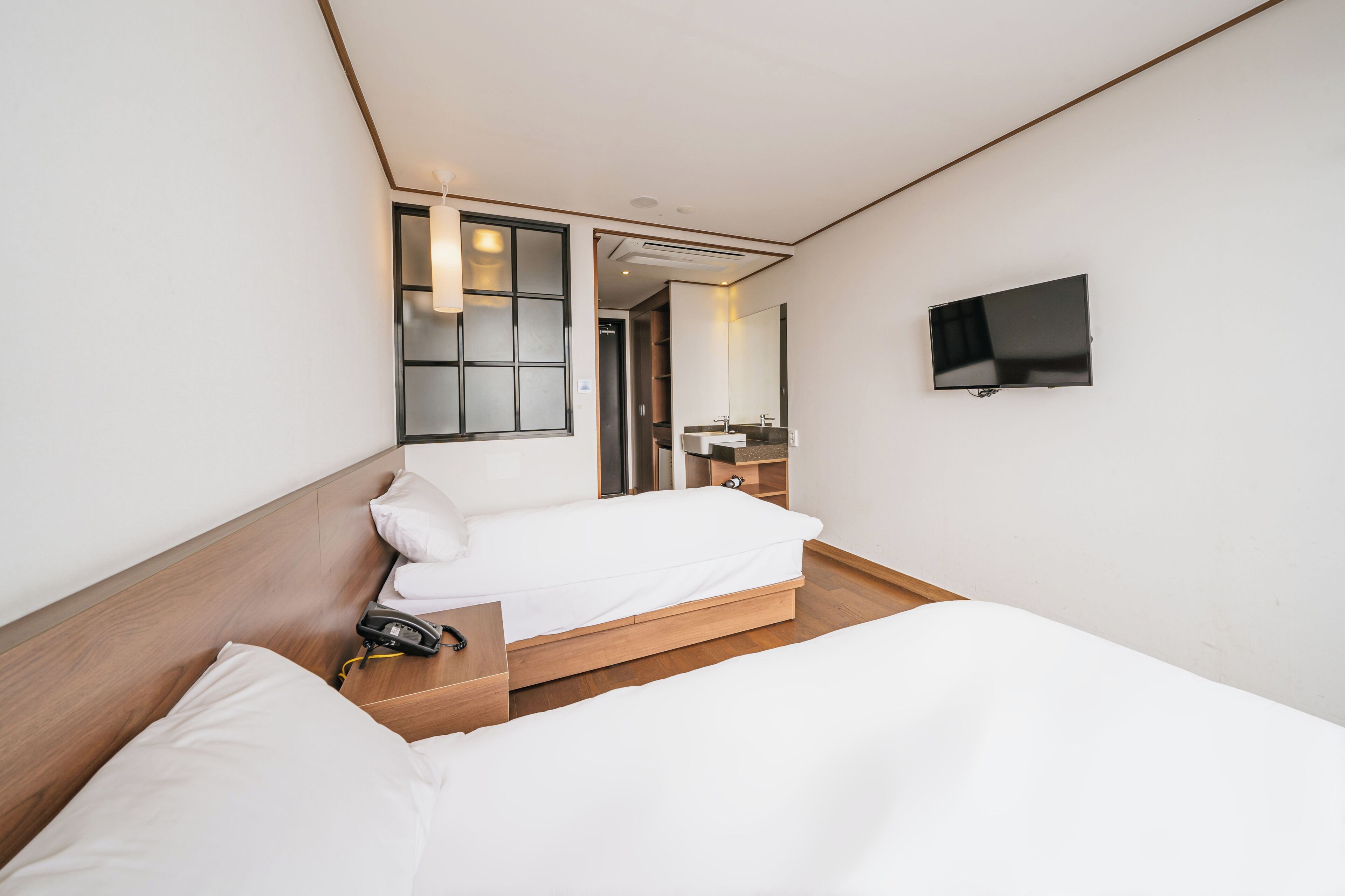 Habitación de hotel con dos camas, televisión, espejo y un baño pequeño.