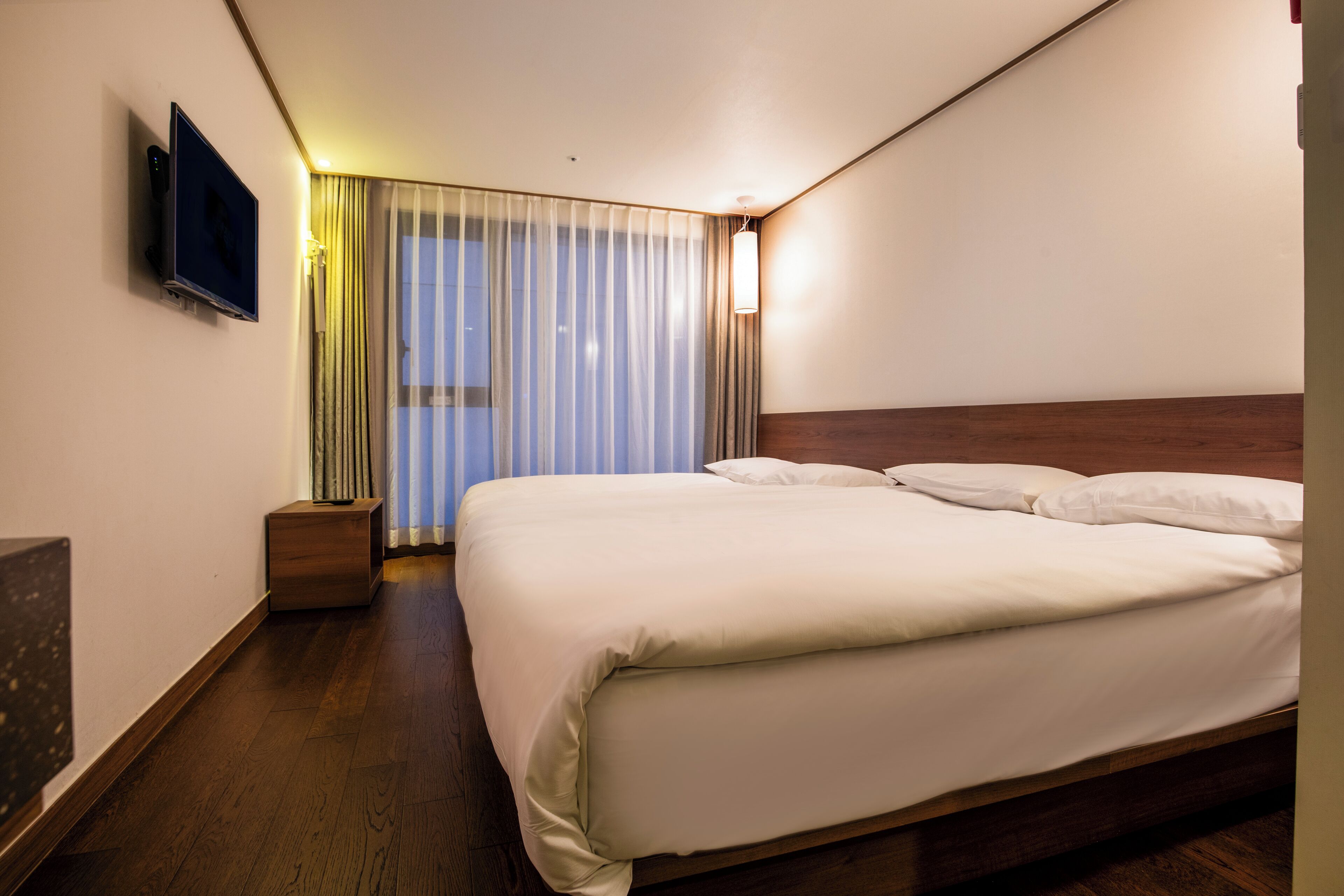 Hotelkamer met een groot bed, een flatscreen televisie aan de muur, een nachtkastje en een raam met gordijnen.