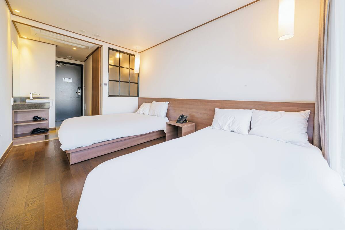 Ein Hotelzimmer mit zwei Betten, einem hölzernen Kopfteil, einem Nachttisch mit Telefon, einem Spiegel und einem kleinen Regal mit einer Lampe.