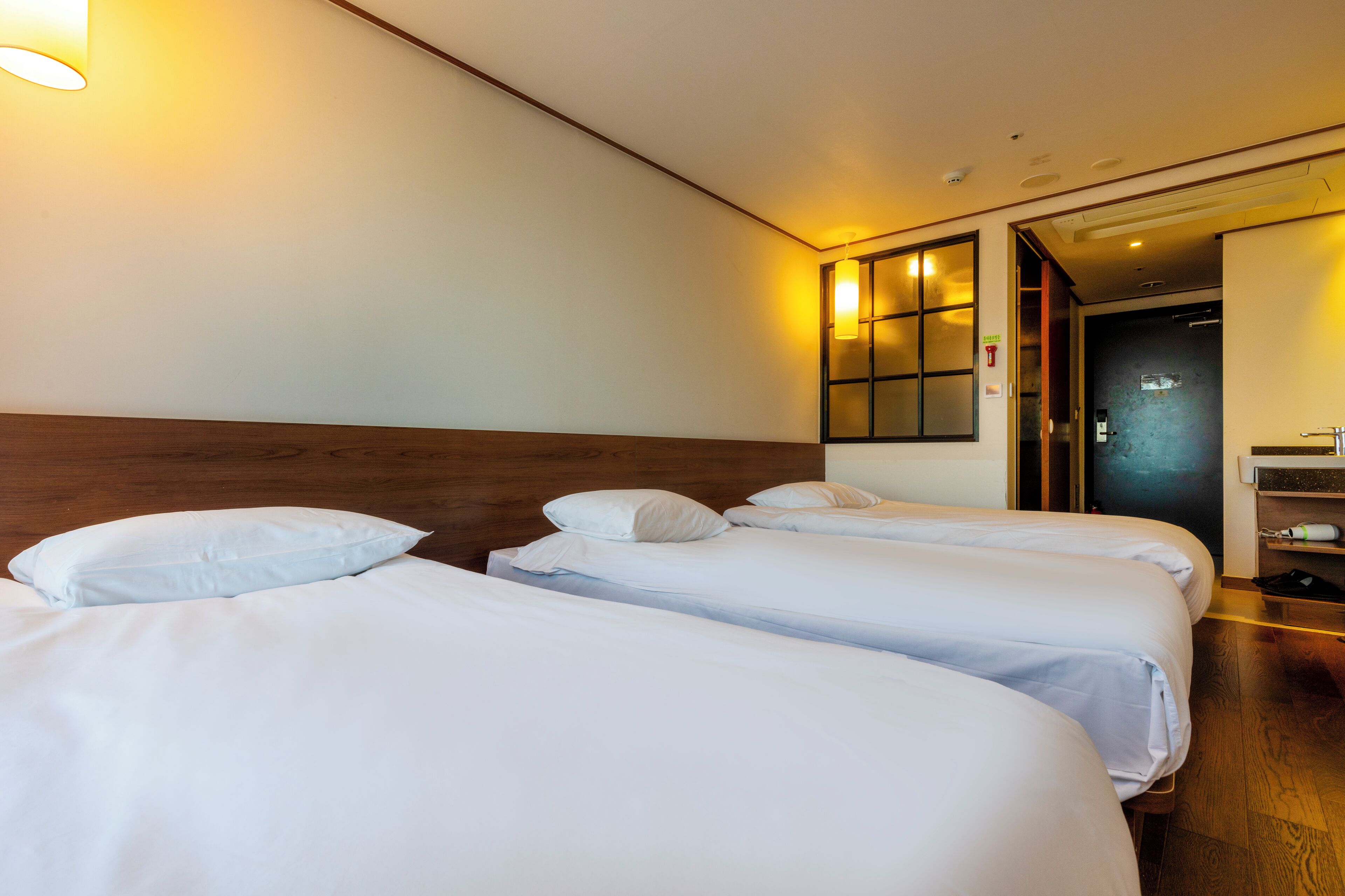A hotel room with two single beds, wooden headboard, and a nightstand with a lamp.