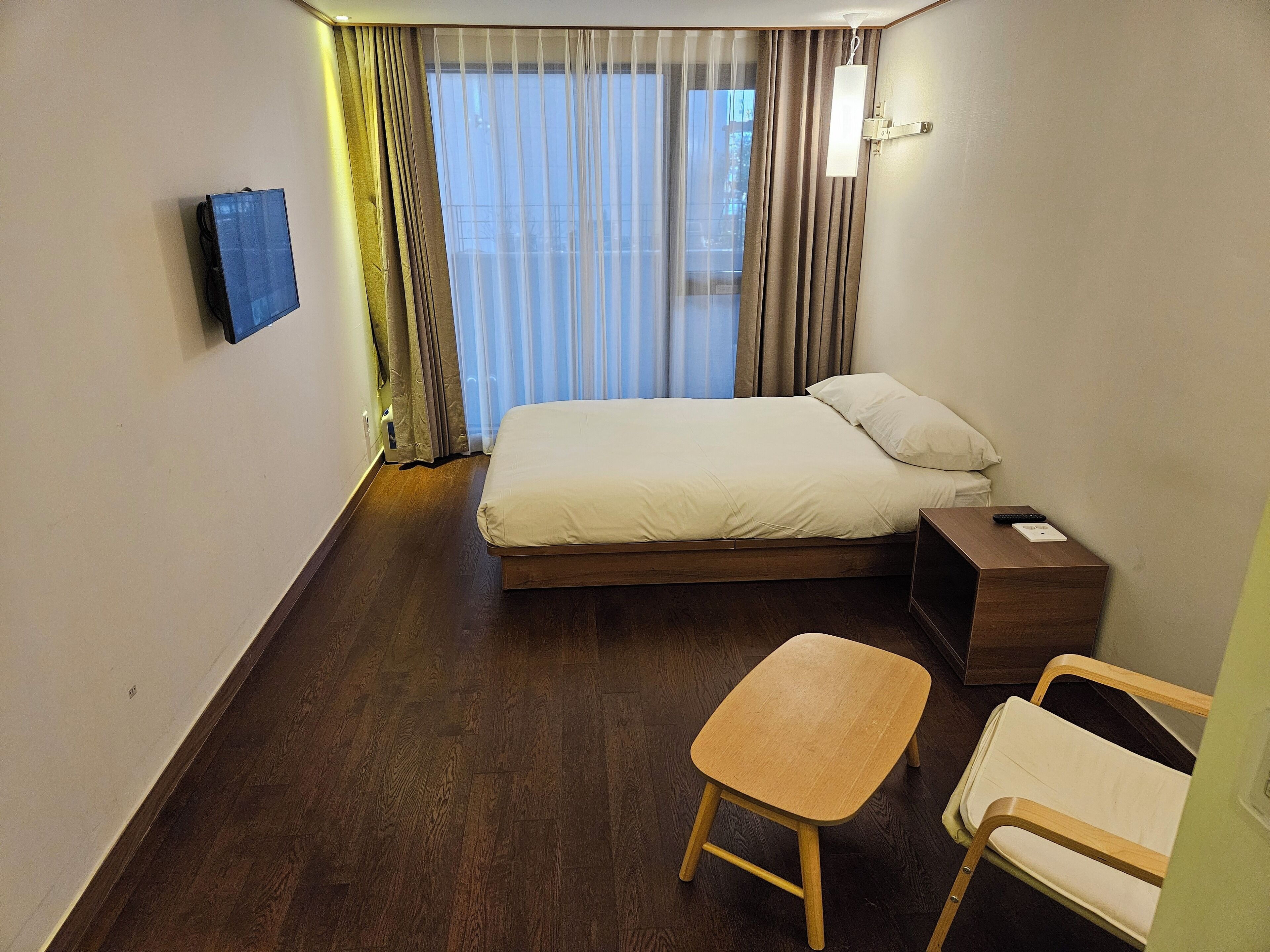 Une chambre d’hôtel équipée d’un lit, d’une table de chevet, d’une chaise et d’un téléviseur fixé au mur.