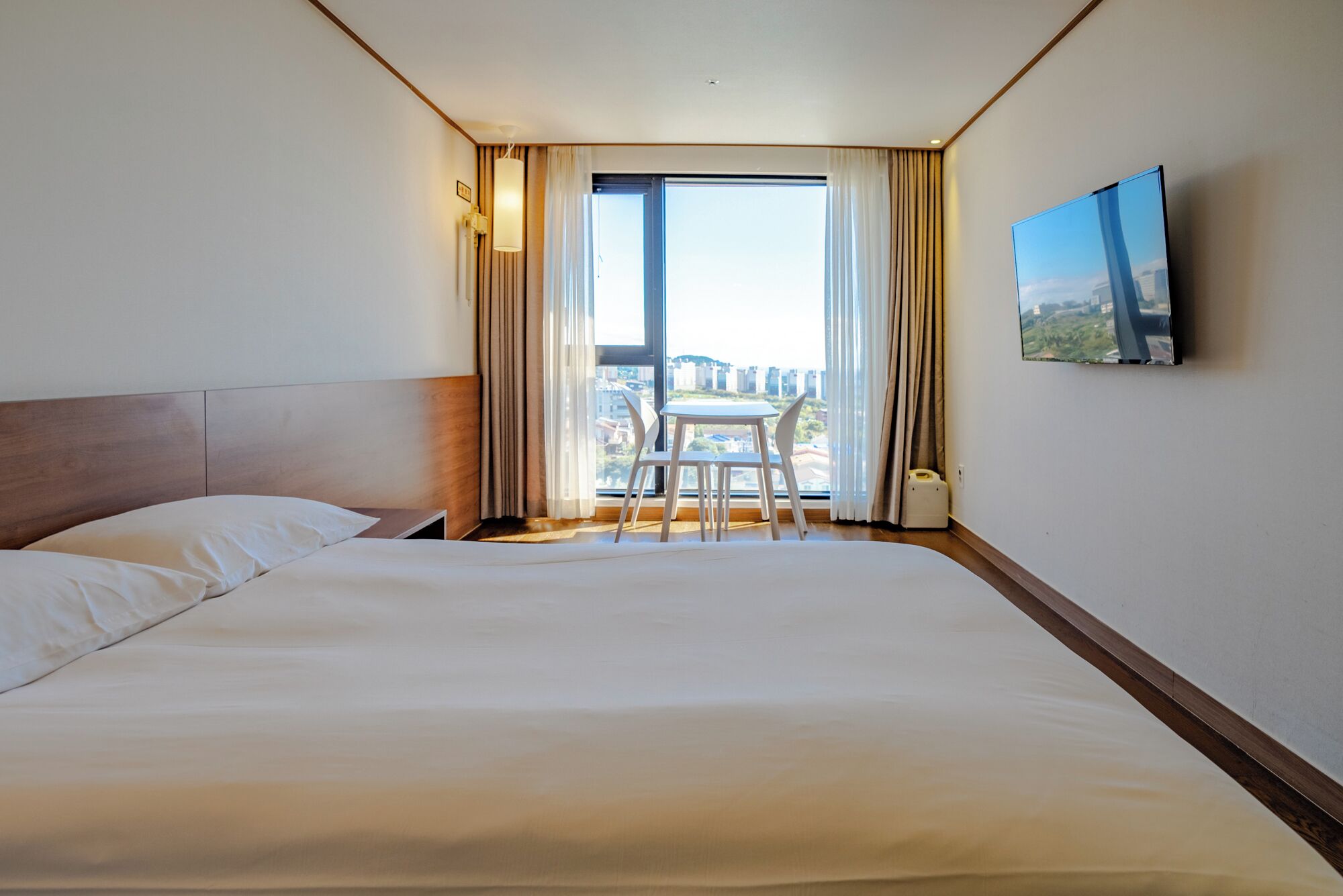 Habitación de hotel con una cama grande, una pequeña mesa con sillas, un televisor en la pared y una ventana con cortinas.