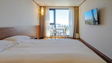 Habitación de hotel con una cama grande, una pequeña mesa con sillas, un televisor en la pared y una ventana con cortinas.