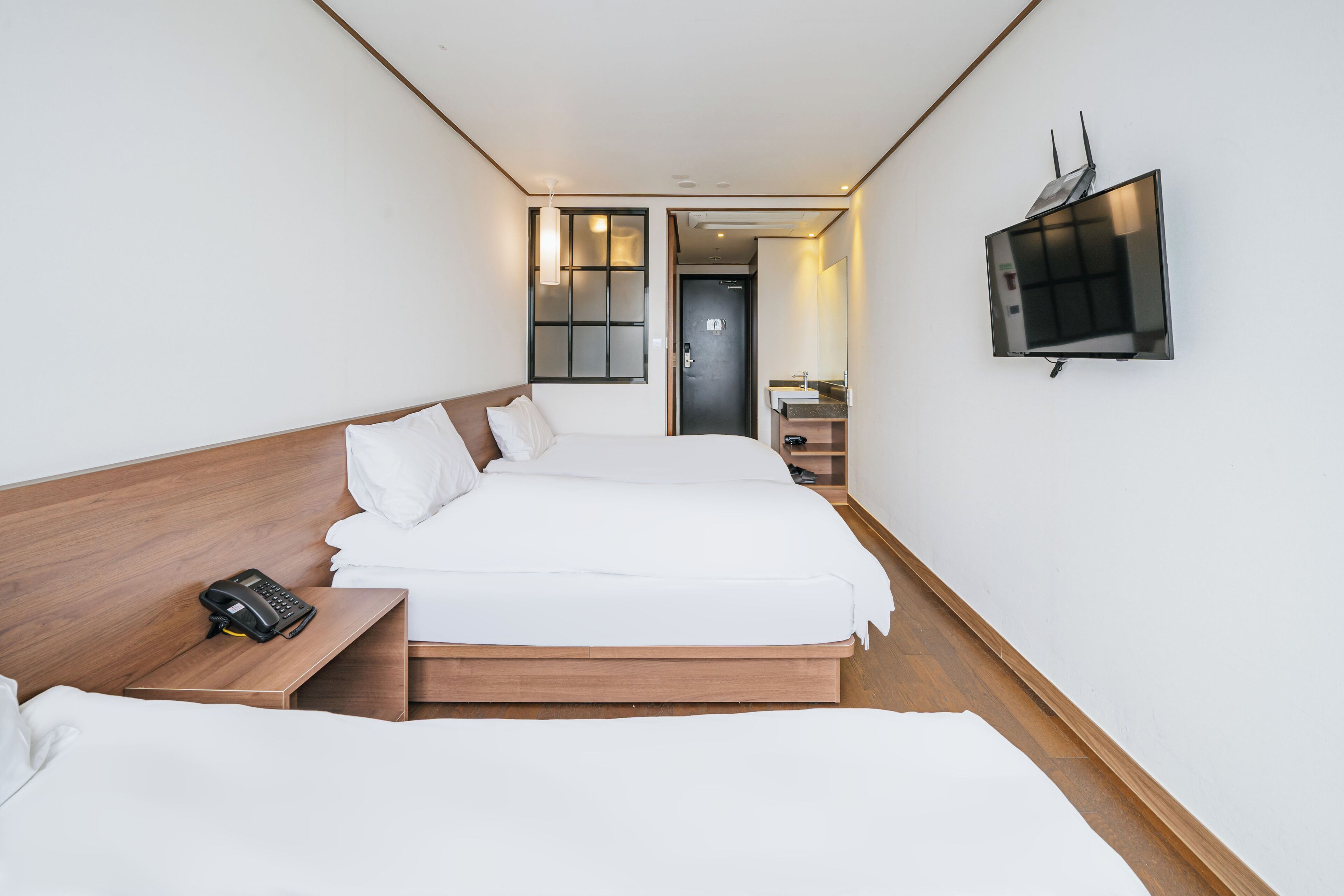 Una habitación de hotel con una cama grande, una mesita de noche con teléfono, un televisor montado en la pared y una puerta que da a un baño.