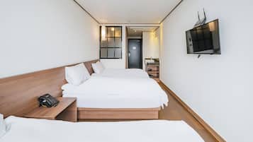 Una habitación de hotel con una cama grande, una mesita de noche con teléfono, un televisor montado en la pared y una puerta que da a un baño.