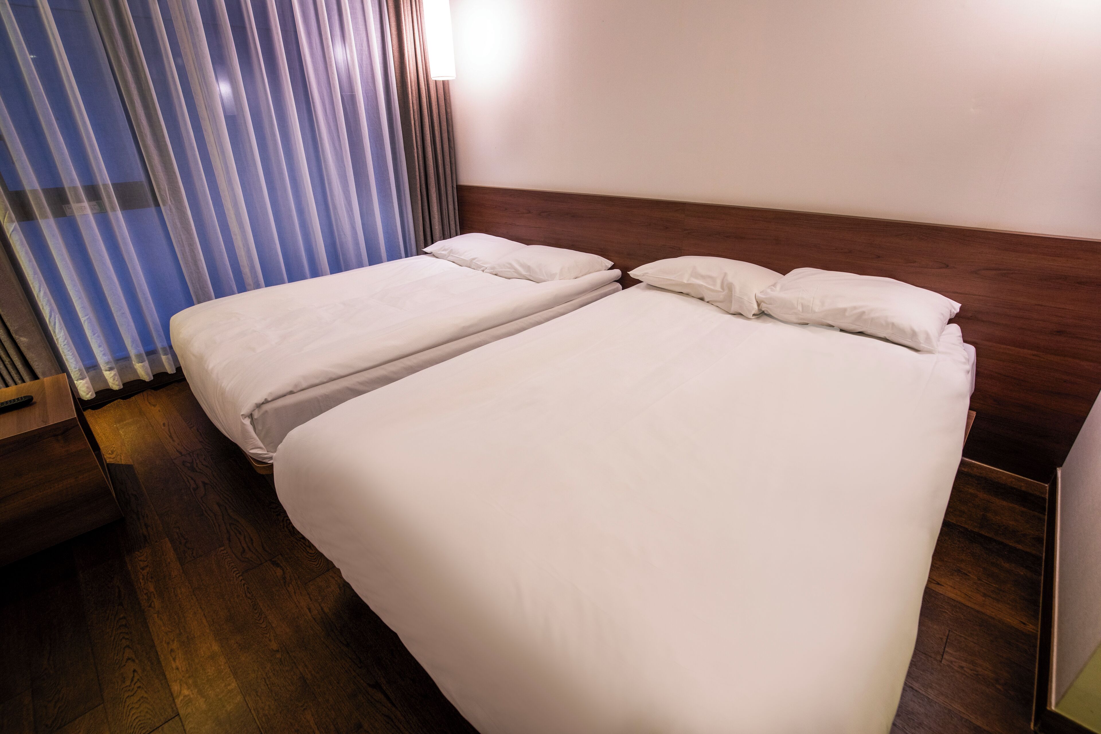 A double bed with white linens, a wooden headboard, and a nightstand with a remote control.