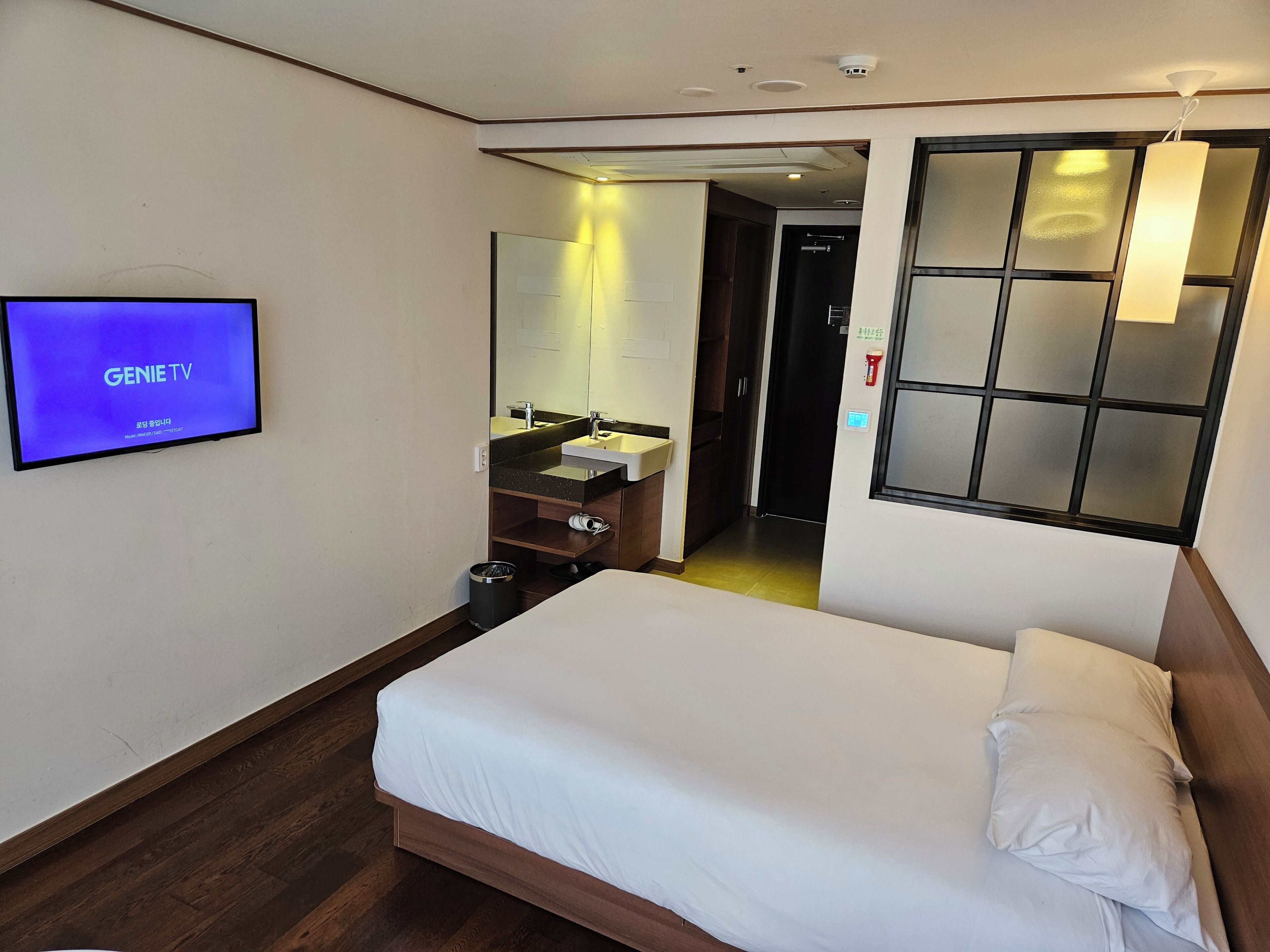 A hotel room with a bed, a TV displaying 'GENIE TV', a bathroom with a mirror, sink, and toilet.