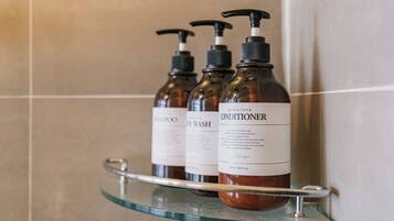 Three bottles of conditioner on a glass shelf in a bathroom.