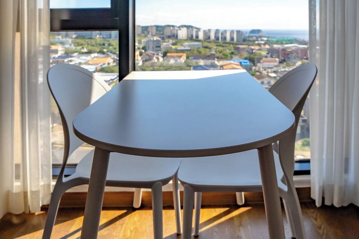 Ein Essbereich mit Tisch und Stühlen, großen Fenstern und Blick auf die Stadt sowie Holzboden.