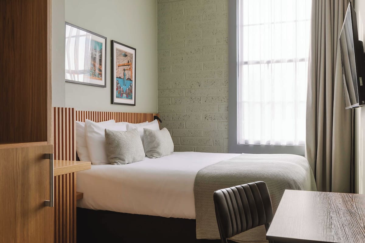 A hotel room with a bed, a wooden headboard, a table, and a TV.