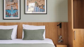 Habitación de hotel con cabecera de madera, dos almohadas verdes, ropa de cama blanca y dos cuadros en la pared.