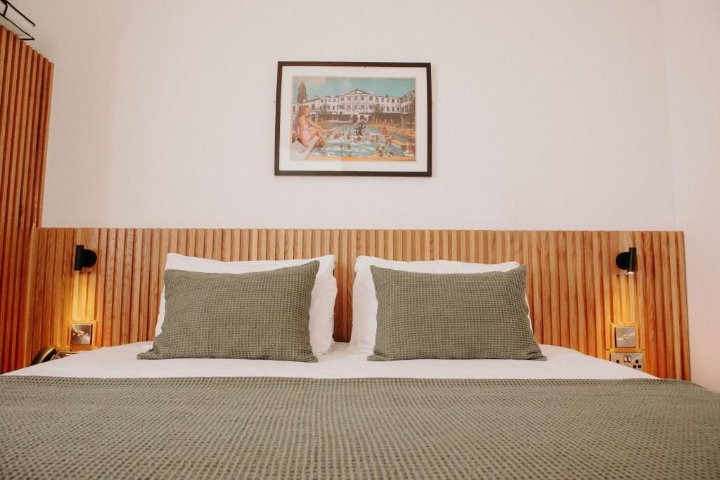 A hotel room with a bed, two pillows, a framed picture on the wall, and wooden paneling.