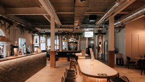 Zona de bar moderna con una barra larga, taburetes y plantas colgantes.