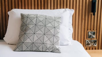 Een bed met een sierkussen met een geometrisch patroon en een effen wit kussen, voor een houten hoofdbord.