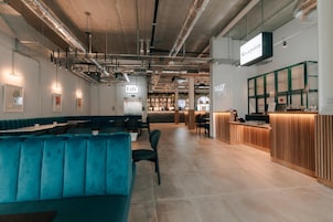 Un restaurante moderno con asientos color turquesa, un mostrador de recepción y conductos expuestos.