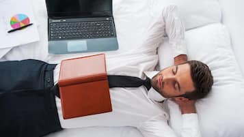 A person lying on a bed with a laptop and a notebook beside them.