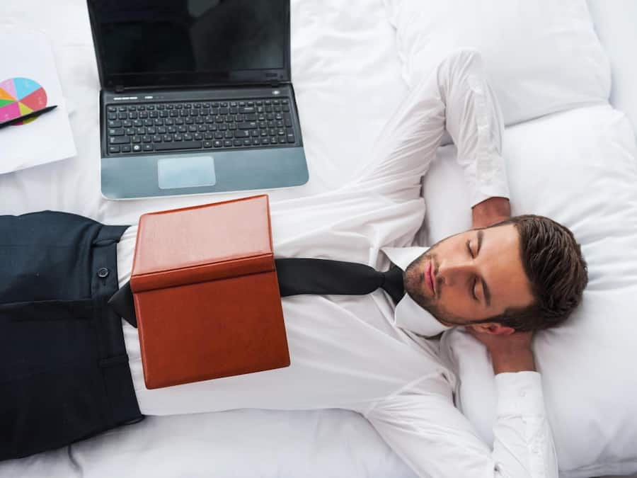 A person lying on a bed with a laptop and a notebook beside them.