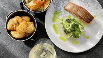 Un plato de salmón, un bol de patatas y una copa de vino blanco sobre una superficie oscura.