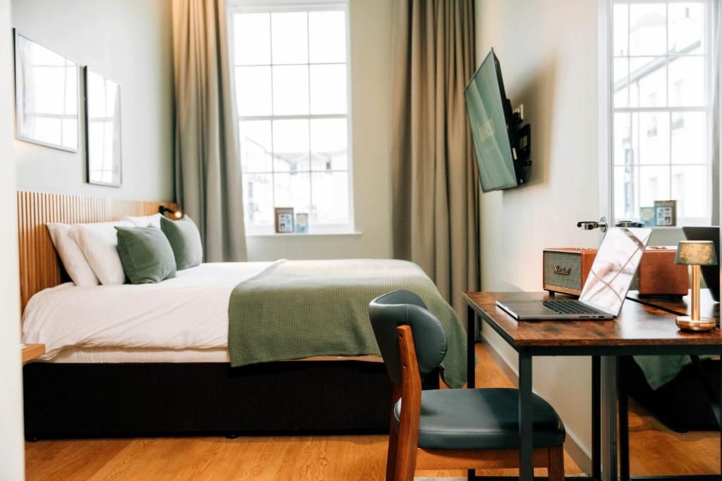 A hotel room with a bed, a desk with a laptop, a television, and a chair.
